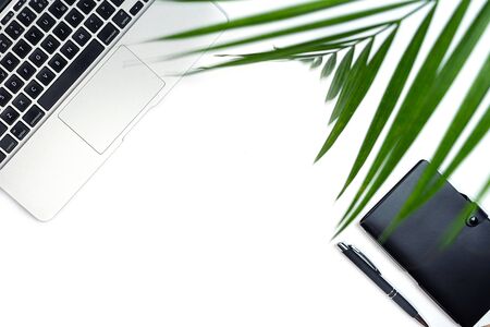 Top view of white office desk with laptop, notebook, palm leaf and supplies. Working from home...