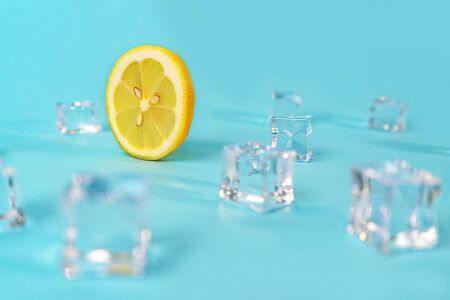 Creative layout made of yellow lemon wheel and ice cube on blue color background. Trendy summer pattern. Minimal fashion concept. Close up.の写真素材
