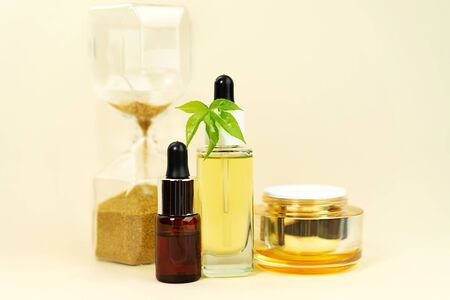 Glass bottles with herbal CBD oil, THC tincture, cream, hemp leaf and hourglass on pastel beige background. Flat lay, minimal style. Cosmetics CBD oil. Essential natural oils for face and body.の写真素材