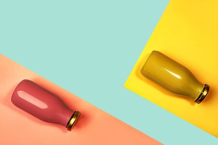 Bottles of multicolored juices or smoothies on yellow, pink coral and trendy mint green blue...