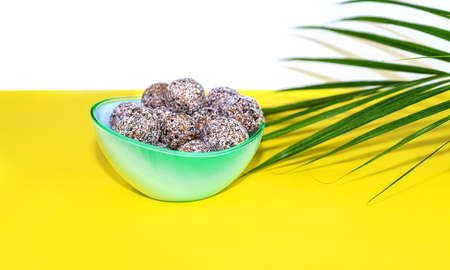 Protein peanut butter energy bites or energy balls. Homemade raw chocolate truffles with nuts and in coconut flakes on plate with palm leaf on yellow background.の写真素材
