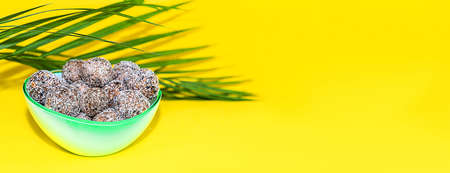 Protein peanut butter energy bites or energy balls. Homemade raw chocolate truffles with nuts and in coconut flakes on plate with palm leaf on yellow background.の写真素材