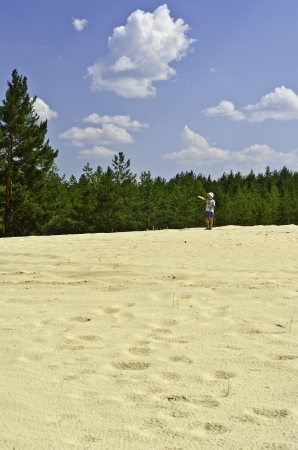 Child on sand-dunes in a pine-wood on a background blue sky with white clouds  の写真素材