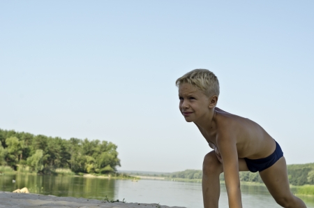 A child does gymnastics on  a river beach on a background the distant forest and sereneの写真素材