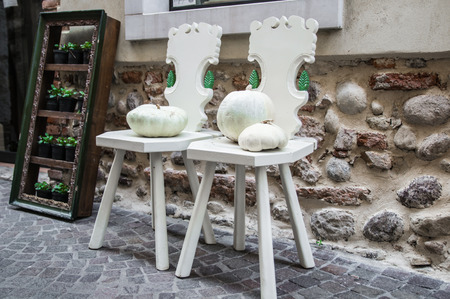 two wooden chairs painted white and two white pumpkins against the wall along a streetの写真素材