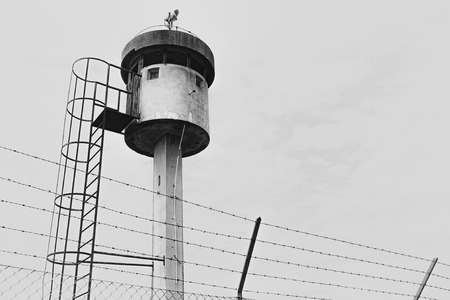 Abandoned watchtower isolated by a net topped with barbed wire.の写真素材