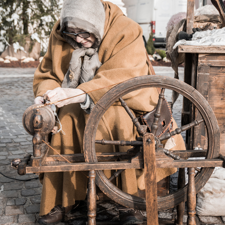 Elderly woman uses the cocoons of silkworms to spin using an old spinning wheel of wood.の写真素材