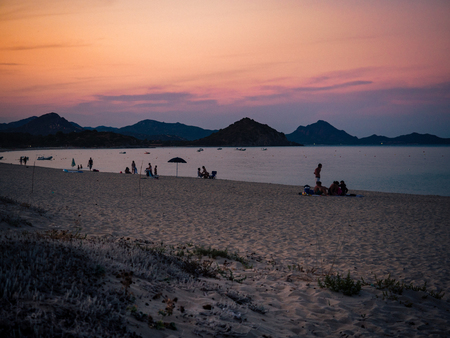 Bathers at sunset on a sandy beach of south Sardinia, Italy.