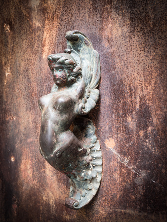 Mermaid-shaped handle of an ancient portal of an old building.の写真素材
