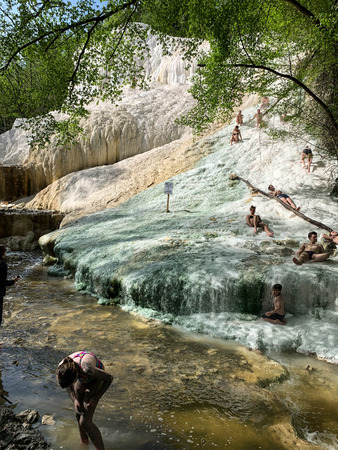 Bagni San Filippo, Italy - April 24, 2019: People rest on the thermal salt waterfalls of the mineral springs of Bagni San Filippo on a sunny day.のeditorial素材