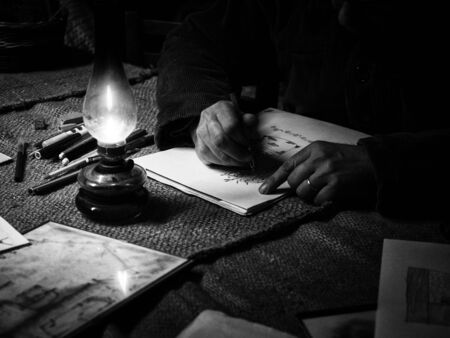 A man draws in a dark and poor room in the light of an oil lantern.の写真素材