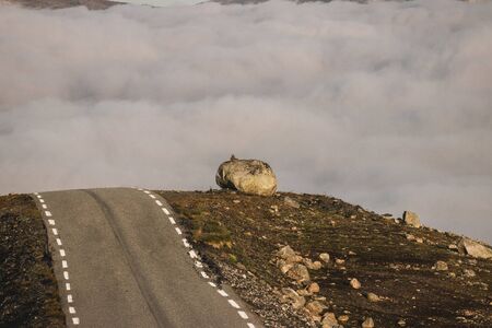 A rock on a mountain next to a road with a cloudy backgroundの写真素材