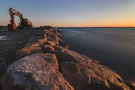 A large digger on a rocky point by the ocean at sunset