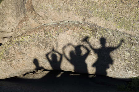 Shadows of happy people with arms raised on rock in sunny dayの写真素材