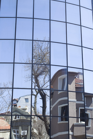 Reflections of old houses and trees in a new glass building