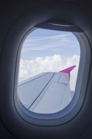 Airplane window and wing in the cloudy skyの写真素材