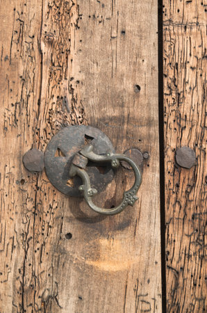 Old medieval metal door knocker on wood worm eaten door closeup