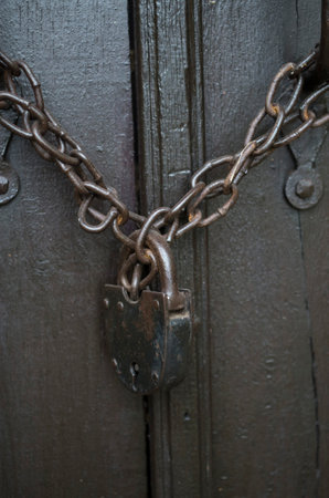 Old rusty chain with a padlock on wooden door closeup