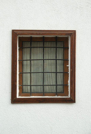 Old small wooden window  with metal grill and curtain on facade in Europeの写真素材