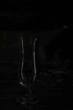 Still life with one single modern transparent and fragile glass on a table with a black backgroundの写真素材