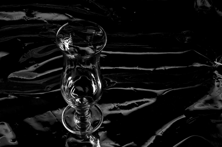 Still life with one empty modern transparent and fragile glass on a table with a black backgroundの写真素材