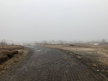 Lonely street in no man's land of Iceland along the Golden Circle Route on a foggy autumn / winter day with typical scenic rural countryside and a cloudy skyの写真素材