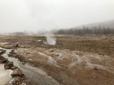 Nordic landscape in Haukadalur valley (Iceland) on a cold autumn / winter day in the geothermal area of The Great Geysir: mud roads, rocks & volcanic nature releasing hot water through geyser springsの写真素材