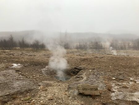 Nordic landscape in Haukadalur valley (Iceland) on a cold autumn / winter day in the geothermal area of The Great Geysir: mud roads, rocks & volcanic nature releasing hot water through geyser springsの写真素材