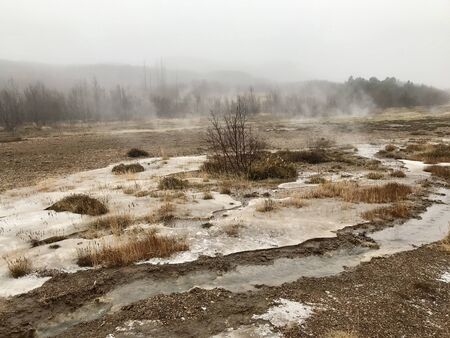 Nordic landscape in Haukadalur valley (Iceland) on a cold autumn / winter day in the geothermal area of The Great Geysir: mud roads, rocks & volcanic nature releasing hot water through geyser springsの写真素材