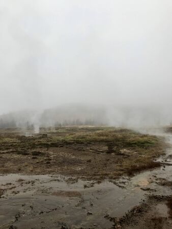 Nordic landscape in Haukadalur valley (Iceland) on a cold autumn / winter day in the geothermal area of The Great Geysir: mud roads, rocks & volcanic nature releasing hot water through geyser springsの写真素材
