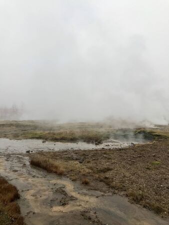 Nordic landscape in Haukadalur valley (Iceland) on a cold autumn / winter day in the geothermal area of The Great Geysir: mud roads, rocks & volcanic nature releasing hot water through geyser springsの写真素材