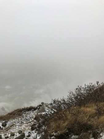 End of the world feeling at the cliffs of the Gullfoss Waterfall in Iceland: Frosted foggy winter landscape with rocks, cascades in the background and snow covered icelandic scenery in Novemberの写真素材