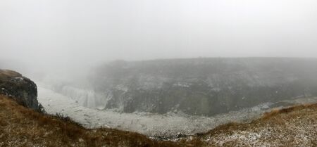 Breathtaking scenery at the Gullfoss Golden Waterfall landmark, a nature attraction in Iceland: Arctic nature with majestic rocks, the Hvita river running in the winter canyon with a cloudy white skyの写真素材