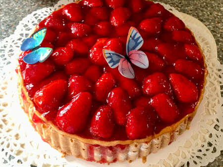 Freshly backed homemade strawberry cake with gelatin decorated with colorful butterflies sitting on a white table in the backyard looking deliciousの写真素材