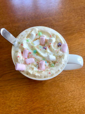 Still life closeup of a breakfast home indulgence of a cup of hot coffee / chocolate / cappuccino decorated with colorful marshmallow confection: Tasty beverage with calories on a brown wooden tableの写真素材