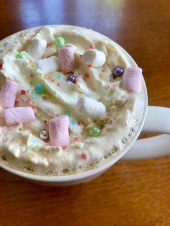 Still life closeup of a breakfast home indulgence of a cup of hot coffee / chocolate / cappuccino decorated with colorful marshmallow confection: Tasty beverage with calories on a brown wooden tableの写真素材