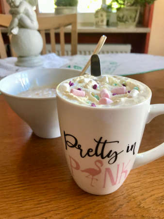 Still life closeup of a breakfast home indulgence of a cup of hot coffee / chocolate / cappuccino decorated with colorful marshmallow confection: Tasty beverage with calories on a brown wooden tableの写真素材