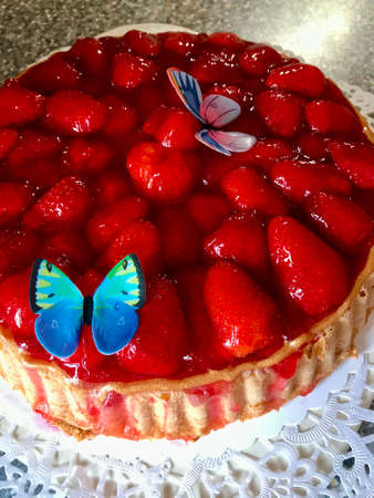 Freshly backed homemade strawberry cake with gelatin decorated with colorful butterflies sitting on a white table in the backyard looking deliciousの写真素材