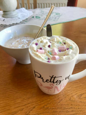 Still life closeup of a breakfast home indulgence of a cup of hot coffee / chocolate / cappuccino decorated with colorful marshmallow confection: Tasty beverage with calories on a brown wooden tableの写真素材