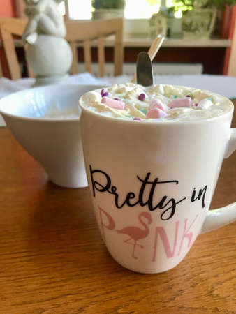 Still life closeup of a breakfast home indulgence of a cup of hot coffee / chocolate / cappuccino decorated with colorful marshmallow confection: Tasty beverage with calories on a brown wooden tableの写真素材
