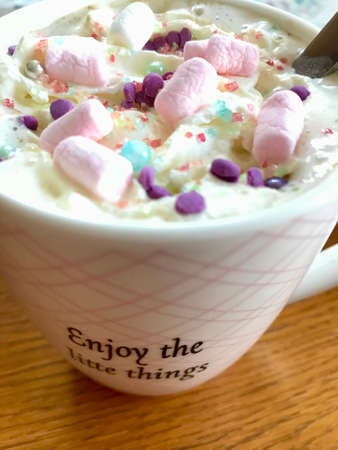 Still life closeup of a breakfast home indulgence of a cup of hot coffee / chocolate / cappuccino decorated with colorful marshmallow confection: Tasty beverage with calories on a brown wooden tableの写真素材