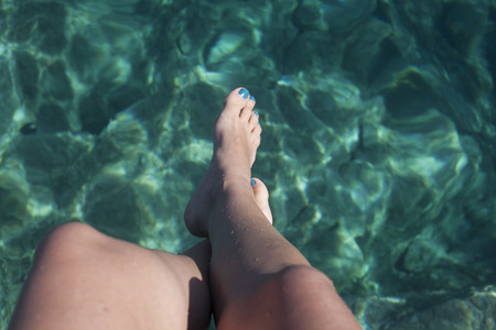a girl sitting above the beautifull Sardinian sea with hanging legs.の写真素材
