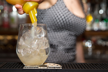 a girl behind a bar is pouring some juice into a glass full of iceの写真素材