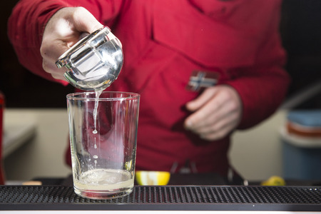 closeup of a barman preparing a cocktail, squeezing a lemon in a glass