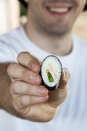 a closeup of a smiling chef holding little piece of italian sushi ( filled with rice, mayonnaise, salad and a slice of ham) in his handの写真素材