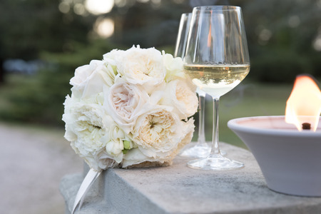 pale pink wedding bouquet under sunset light with two glasses of white wineの写真素材