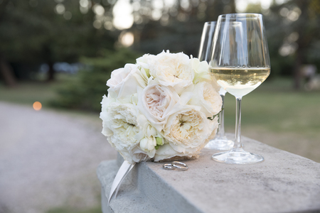 wedding bouquet with wedding rings under sunset light with two glasses of white wine の写真素材