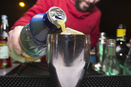 bartender is pouring some fruit juice directly from the plastic bottle into a shaker の写真素材