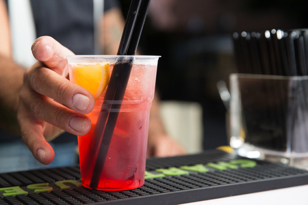 closeup of a barman holding a platic glass on the counter, with a red cocktail in itの写真素材