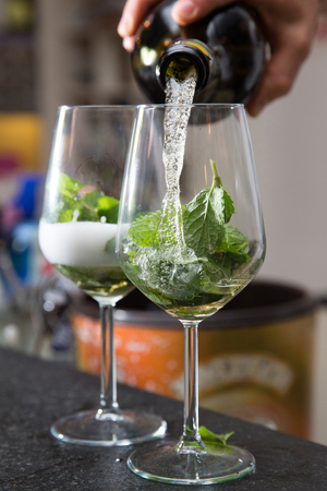 bartender is pouring some sparkling wine into wine glasses with mint leafs  の写真素材